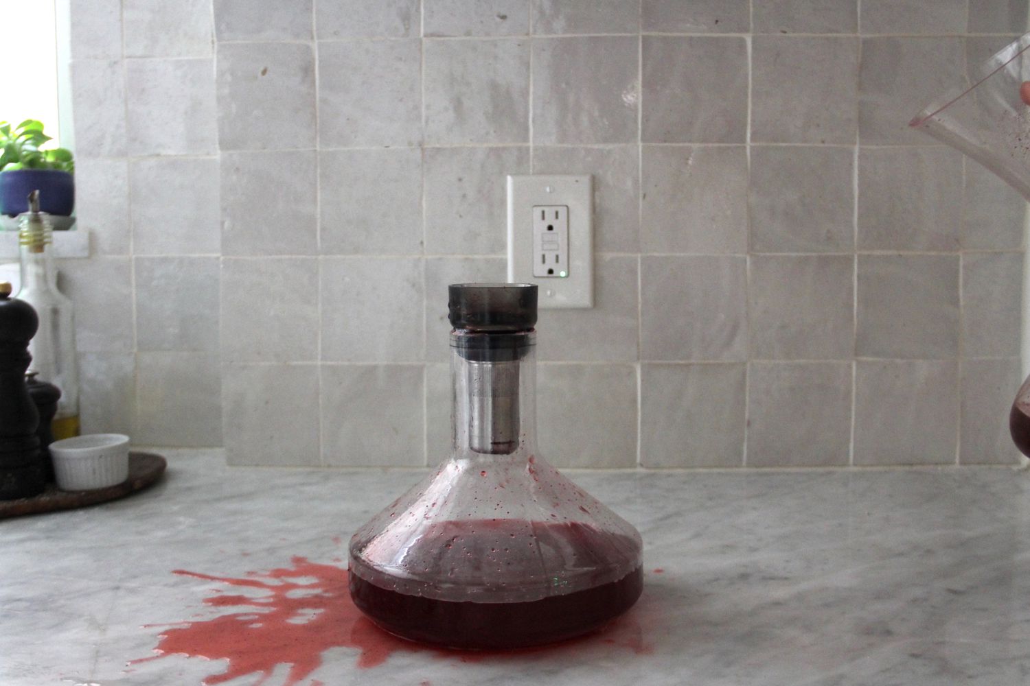 Spilled red wine on a marble counter next to the Rabbit Pura wine decanter