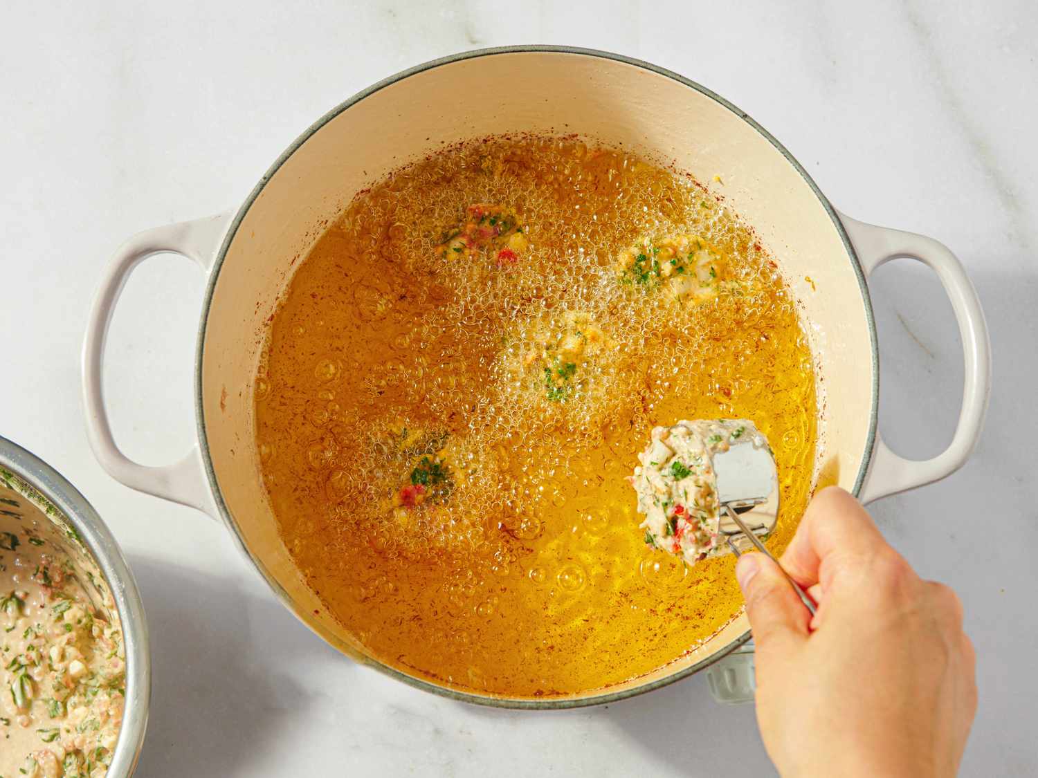 Scooping a portion of fritter mix into a pan of hot oil for frying