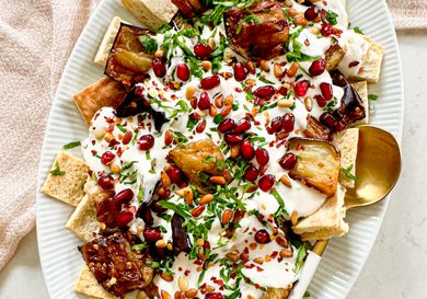 A plated serving of eggplant fatteh garnished with pomegranate seeds parsley and yogurt sauce