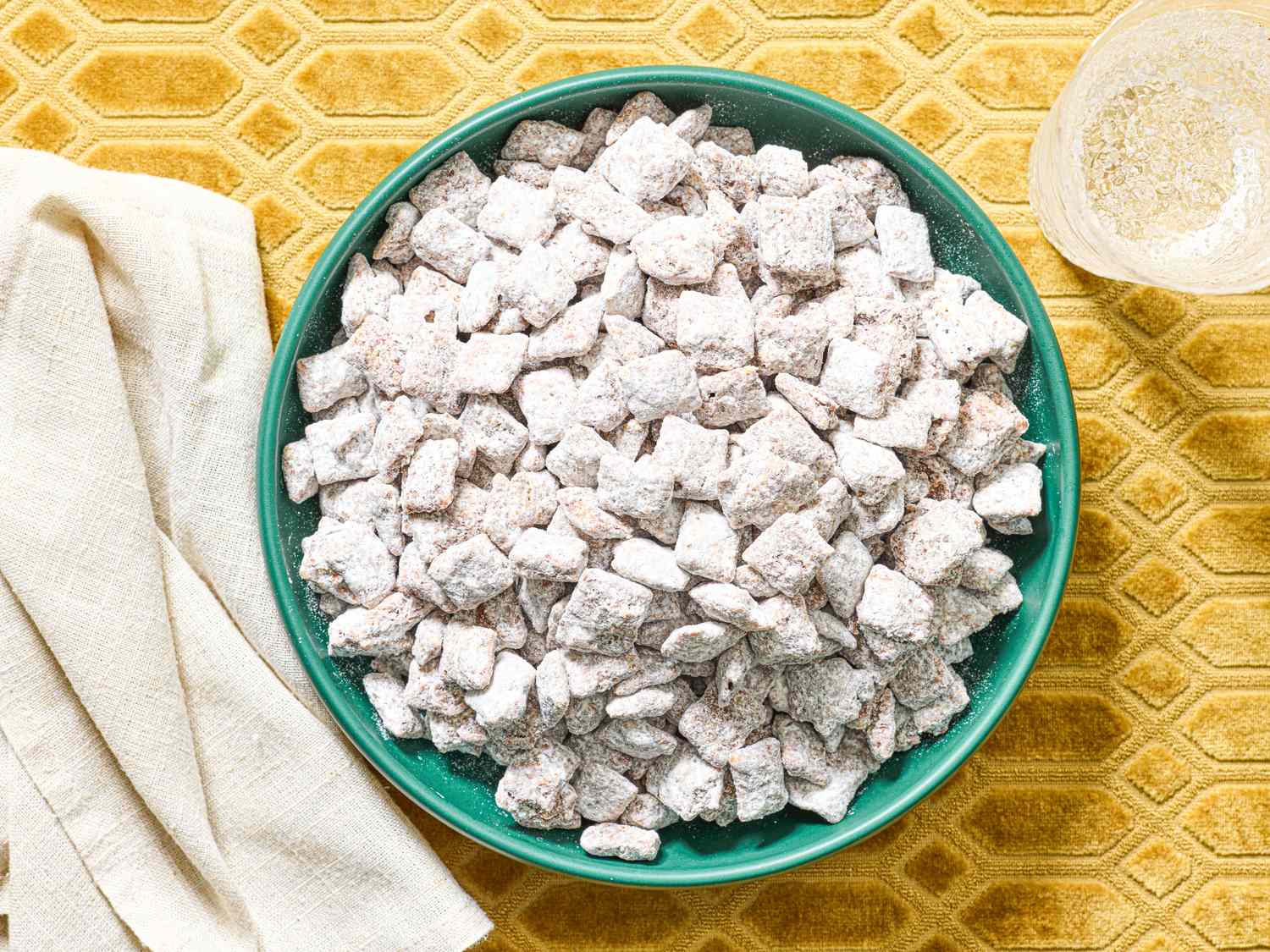 A bowl of powdered sugarcoated snack mix on a textured surface