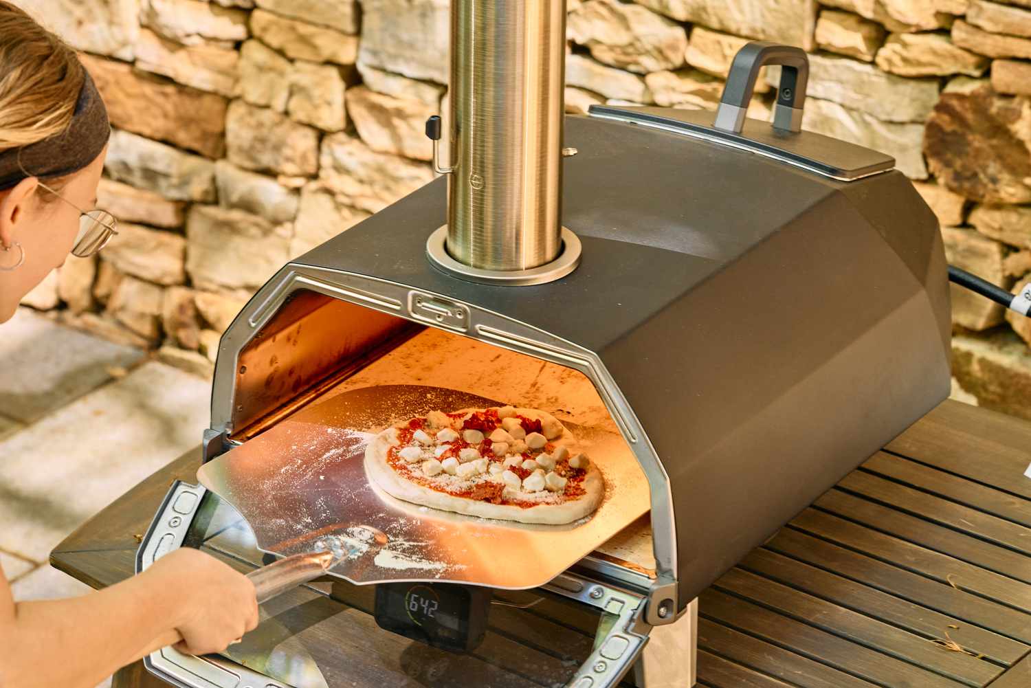 A person places a pizza into the Ooni Karu 2 Pro Multi-Fuel Pizza Oven