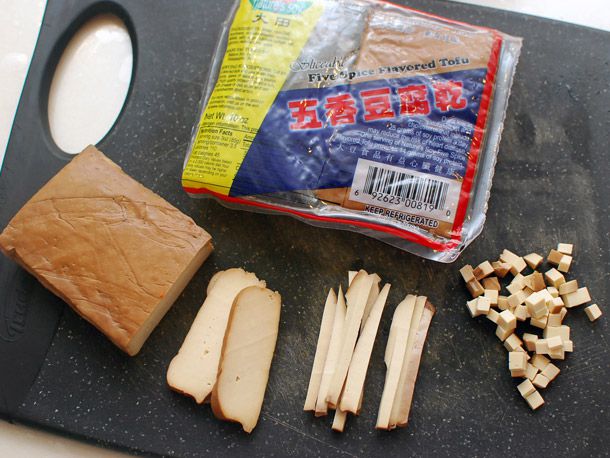 A package of five-spice tofu on a cutting board with a block of it cut into uniform slices, strips, and small dice.