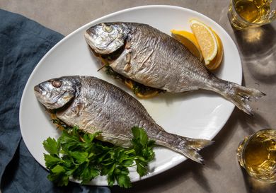Two whole roasted daurade (orata) sit in a platter with some lemon wedges and parsley garnishing the plate