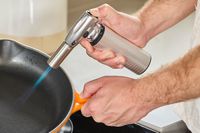 a person using the messermeister torch to heat a skillet