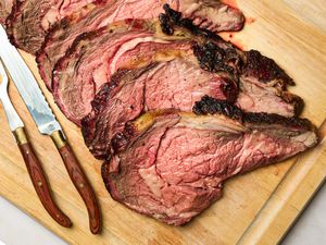 Sliced prime rib on a wooden cutting board with carving utensils nearby