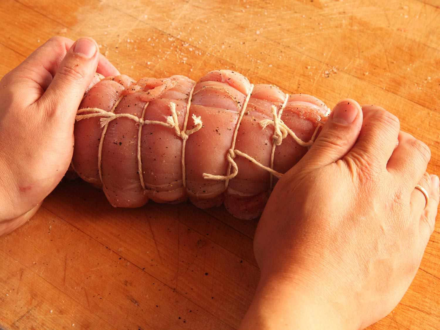 Hands holding two seasoned, raw turkey breast lobes tied together with butcher's twine.