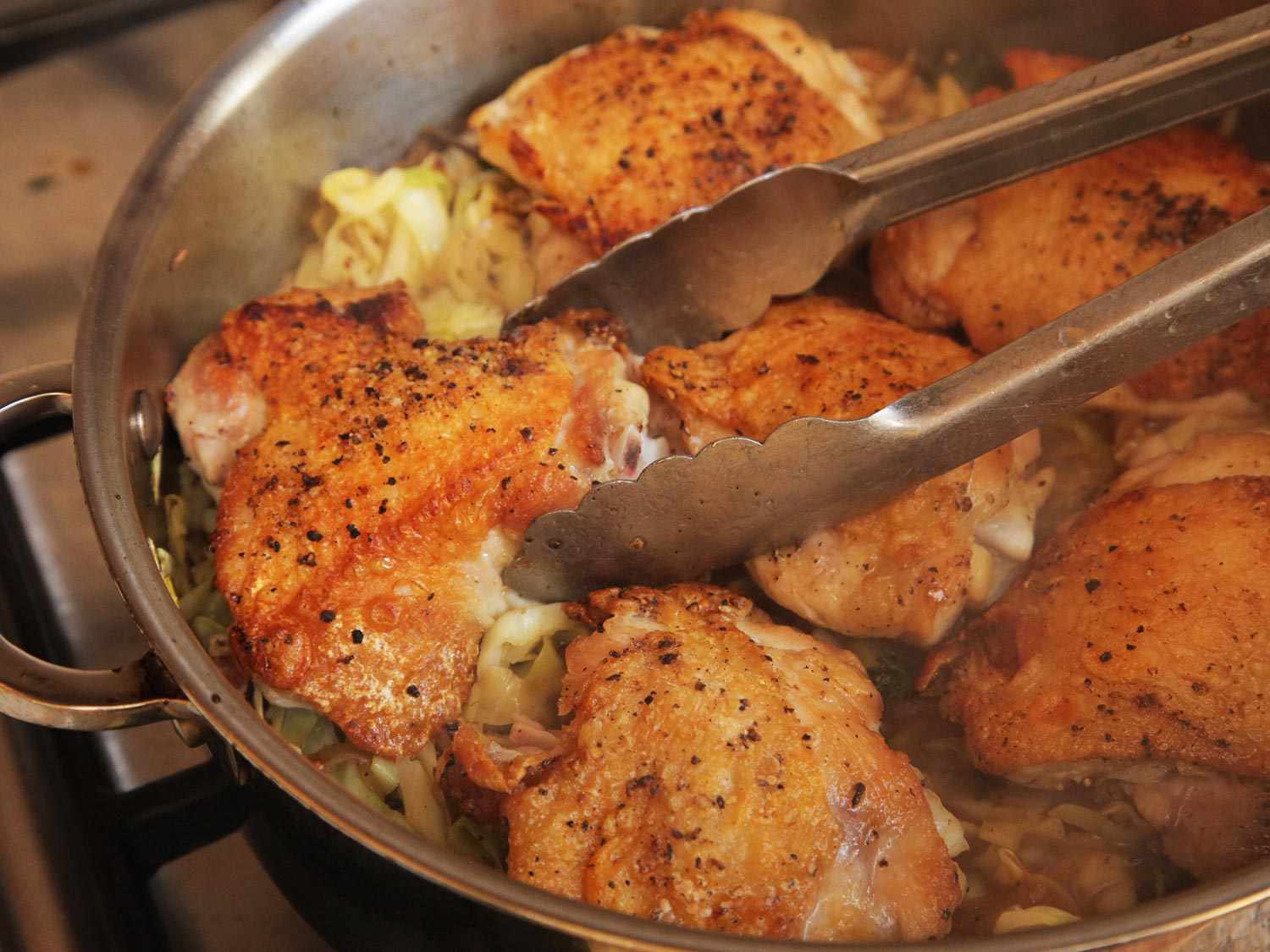 Nestling browned chicken thigh with tongs onto a pan of sauteed cabbage and pancetta 