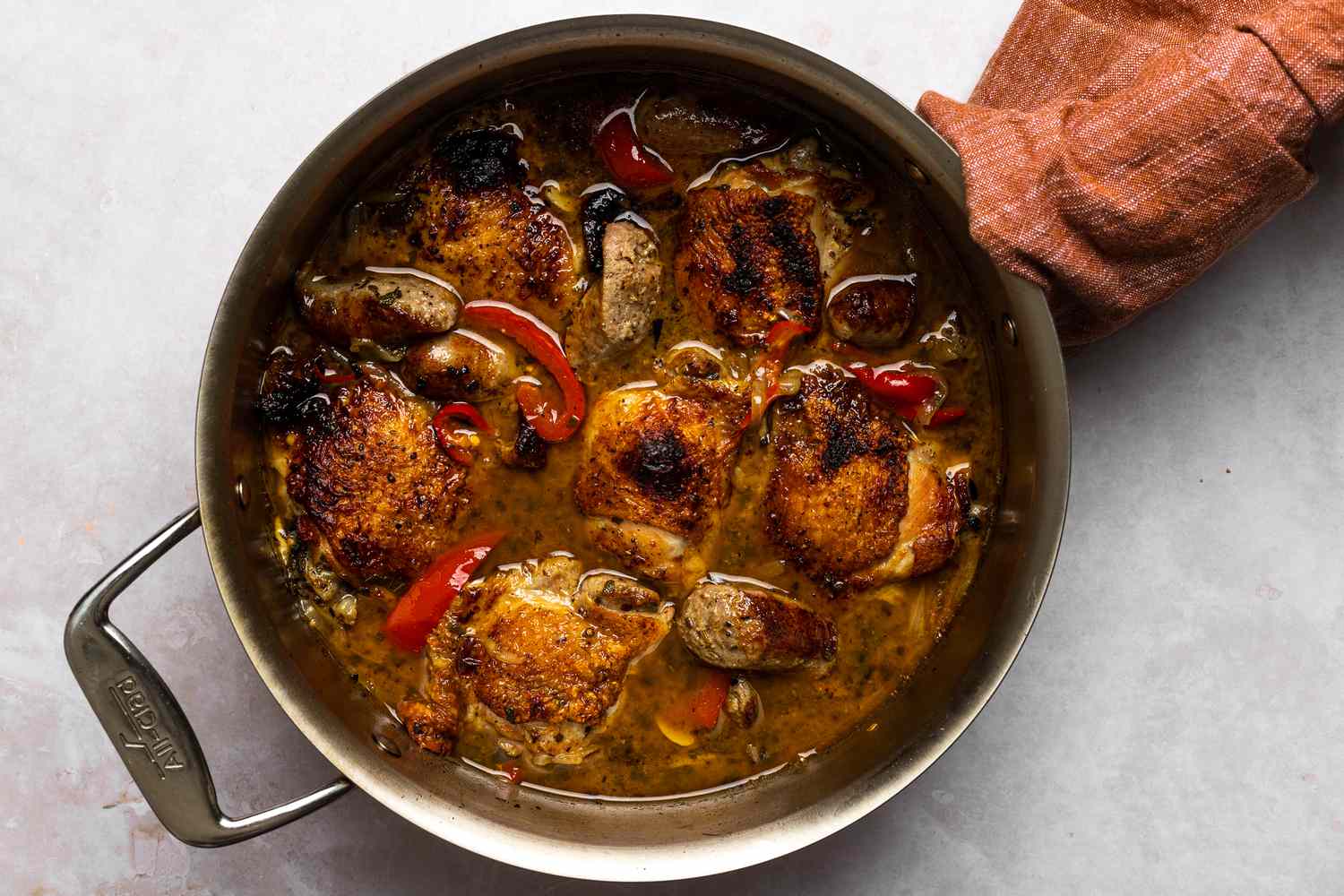 Crispy and tender chicken with sausages and reduced liquid inside of the stainless steel pan.