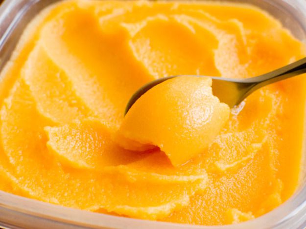 Clementine sorbet is scraped out of a storage container with a spoon.