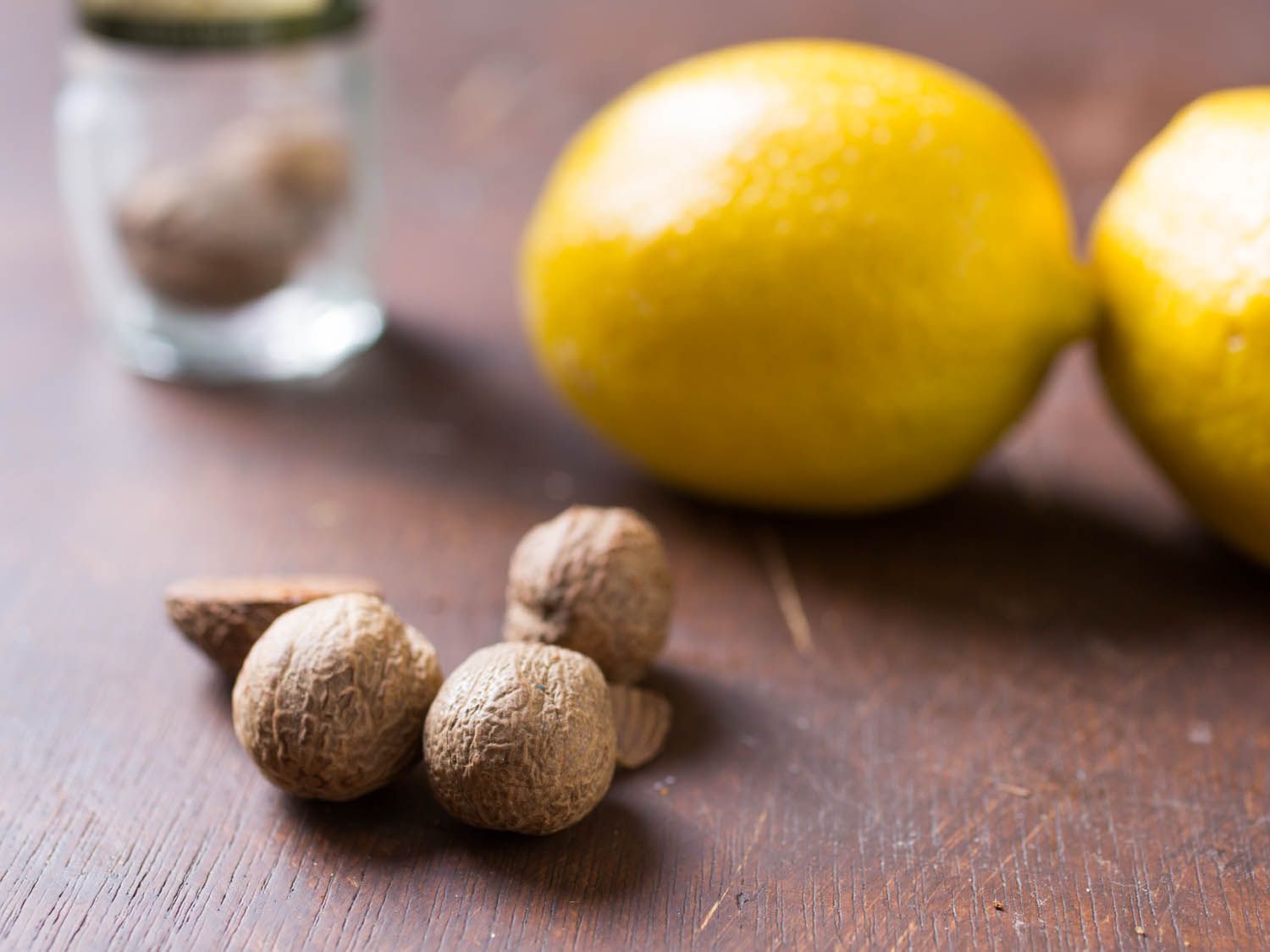 Close-up of whole nutmeg and whole lemons on a wooden surface.