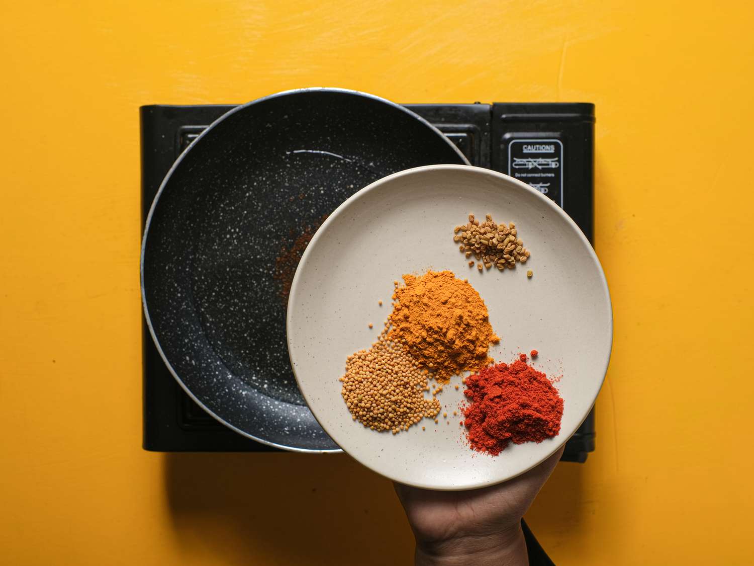 Plate of different spices help above skillet