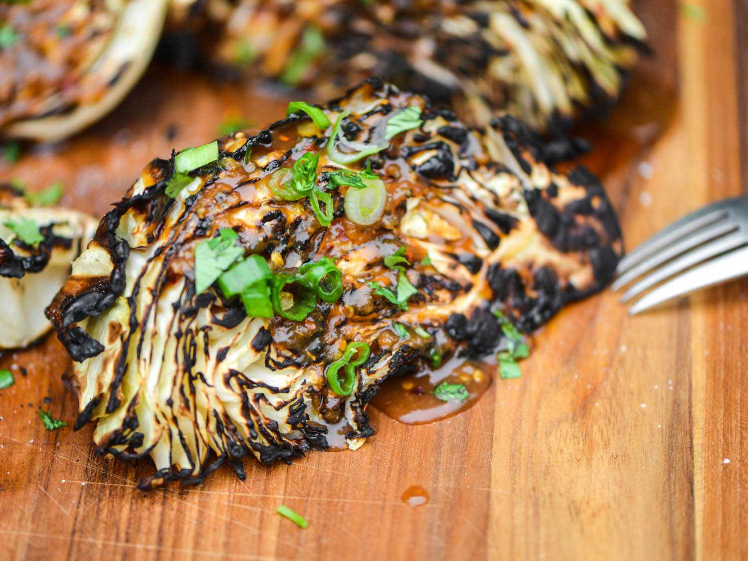 Grilled cabbage wedges on a cutting board, drizzled with ginger-miso dressing and sliced green onions