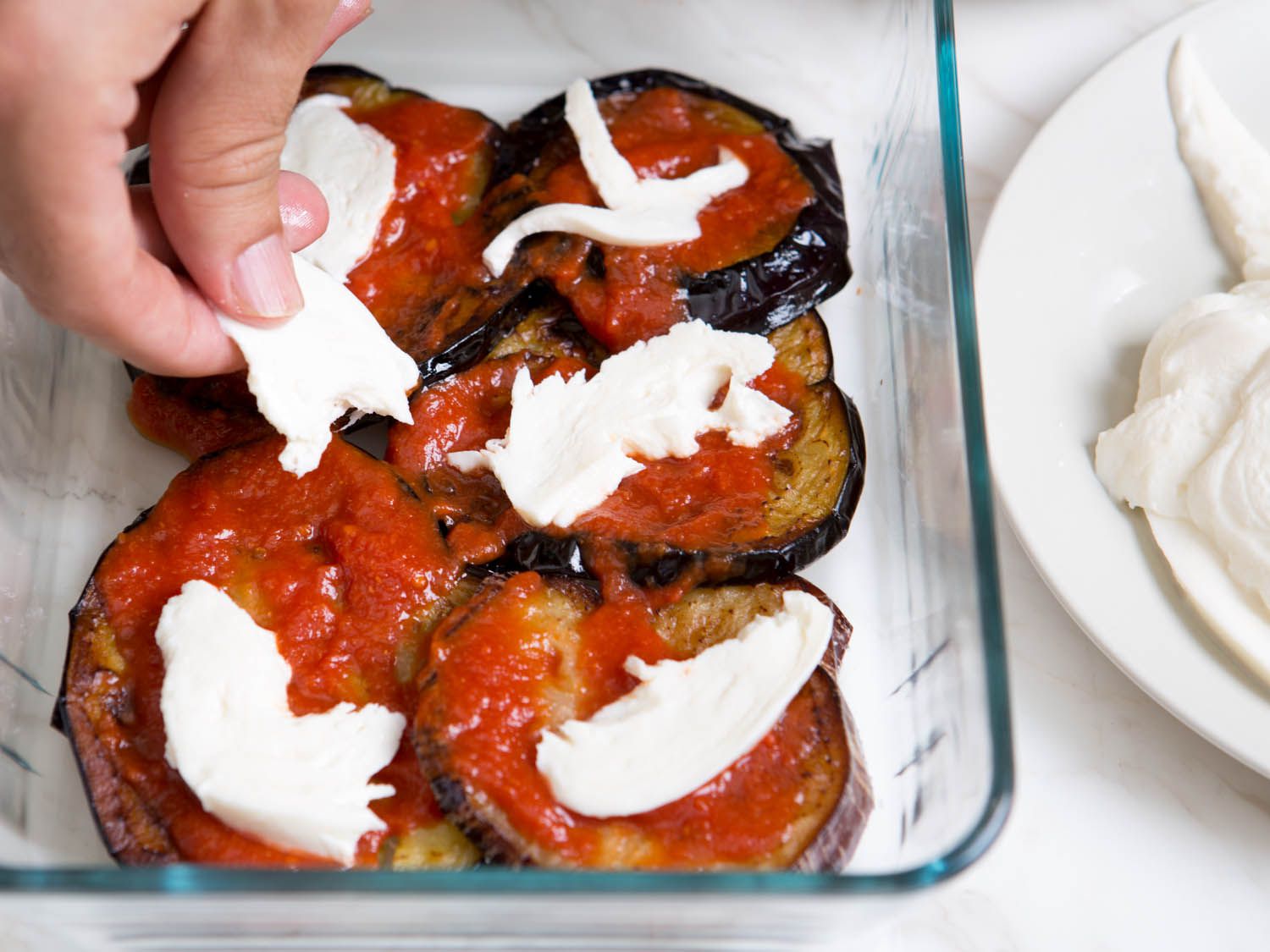 Layering mozzarella pieces on top of tomato sauce and fried egg plant slices. 