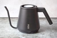 A modern kettle with a spout and a thermometer branded MiiR placed on a textured surface