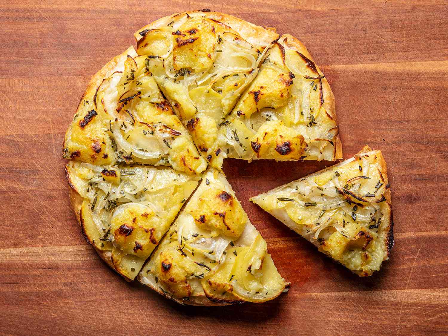 A potato pizza cut into wedges on a wooden cutting board.