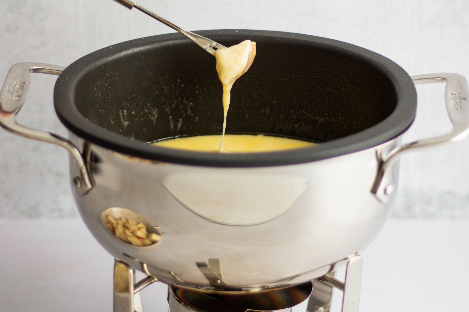 A cube of bread being dunked into cheese fondue.