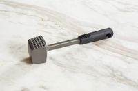 a mallet-style meat pounder with a silicone handle on a marble surface