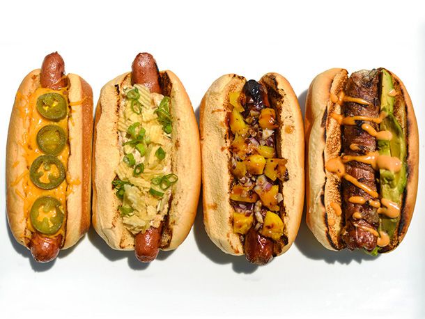 Overhead view of four hot dogs on a white surface, garnished with a variety of topping combinations.