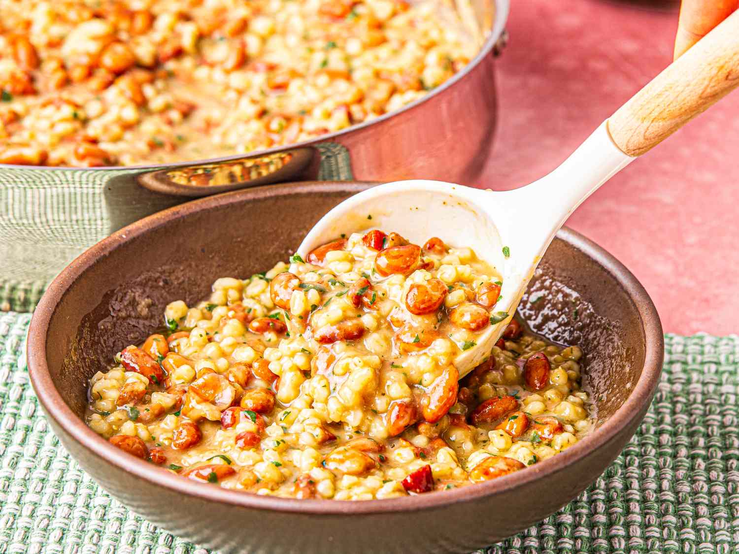 Bowl of barley and cranberry bean soup being served with a spoon dish in a rustic setting