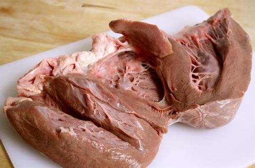 A butterflied raw beef heart on a white cutting board