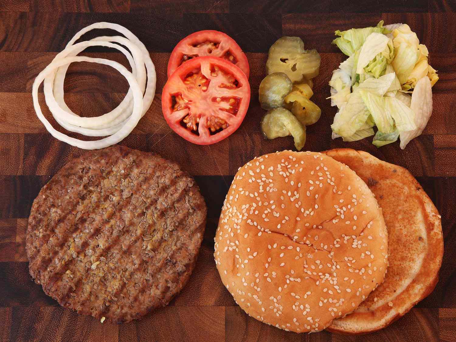 Overhead shot of an un-sauced, cheese-less Whopper that has been disassembled on a cutting board.