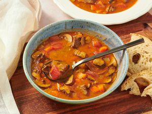 Kansas City Steak soup in bowl on wooden board with spoonful of soup, bread, and another bowl in thebackground