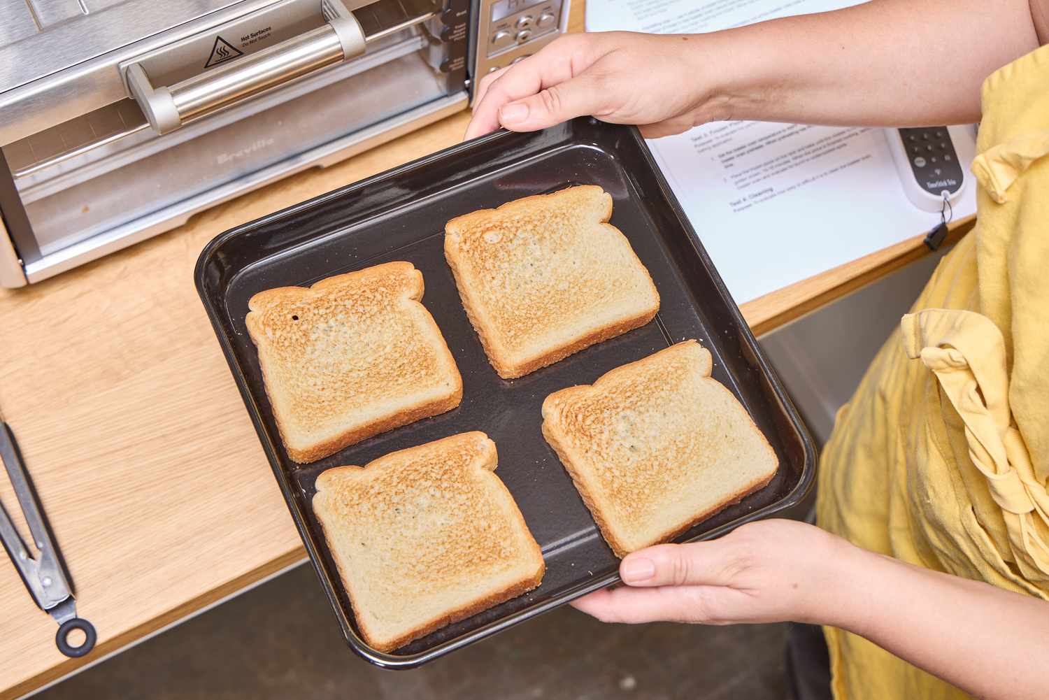 Two hands holding a tray of toast made with the Breville the Mini Smart Oven BOV450XL