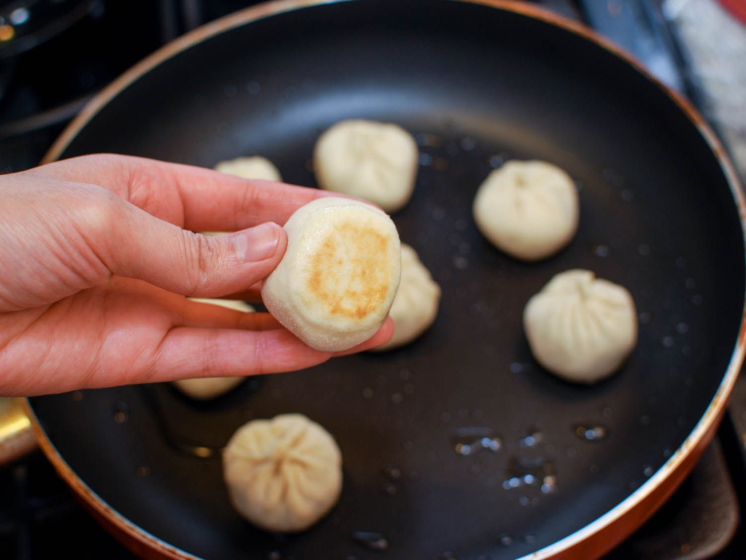 Author holding a sheng jian bao up to inspect the bottom, which is lightly browned.