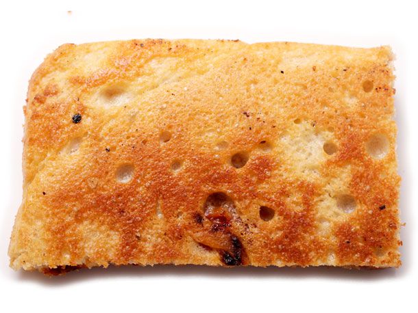 Closeup of an upturned slice of sfincione pizza. The olive oil-fried crust is golden with browned areas.