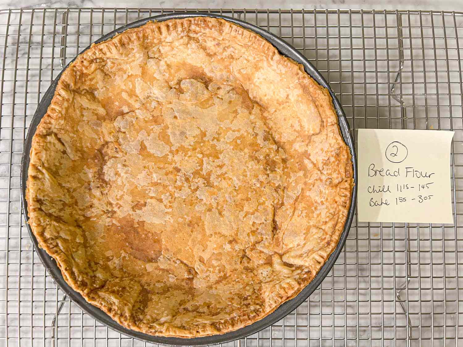 A baked pie crust on a cooling rack with a note labeled 2 describing bread flour and baking instructions