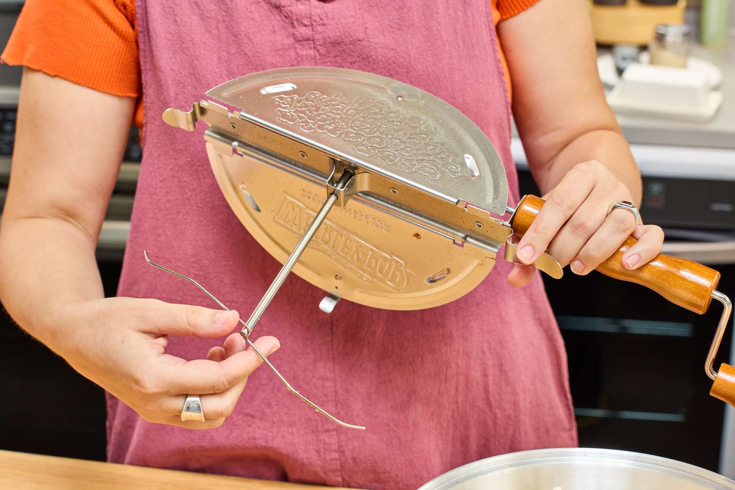 A person touches the stirrer on the Wabash Valley Farms Original Whirley-Pop Popcorn Popper Stainless Steel