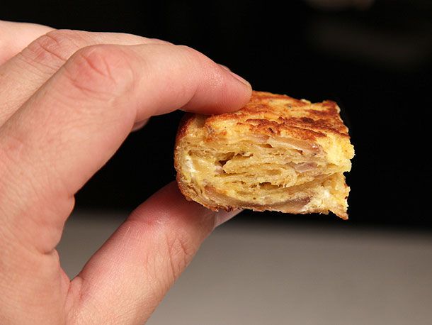 Author holds a piece of the Spanish tortilla up to the camera to show the layers of egg, onion, and chips.