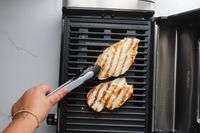 A person flipping grilled chicken on the Hamilton Beach indoor grill