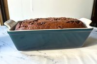 A loaf of chocolate bread in a blue stoneware pan on a marble surface