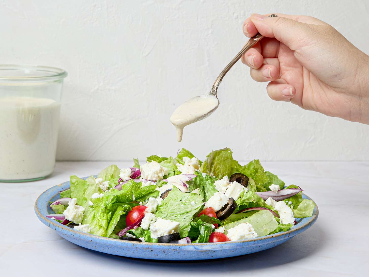 A spoon drizzling dressing onto a green salad with various toppings on a plate