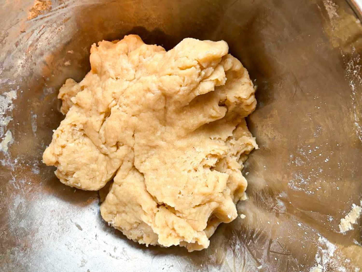 A ball of pie dough in a metal mixing bowl prepared for baking