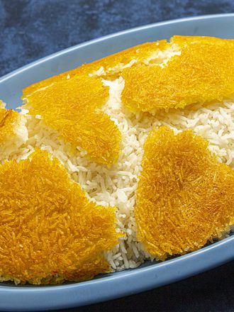 Side angle view of Tahdig arrange on a mound of rice on a blue platter