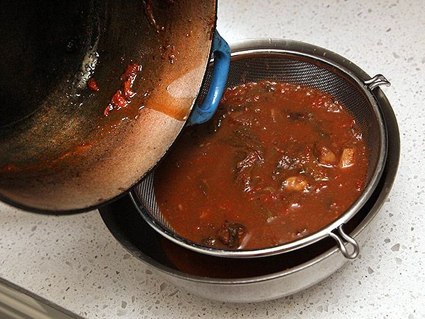 The broth is poured through a fine mesh strainer and into a bowl.