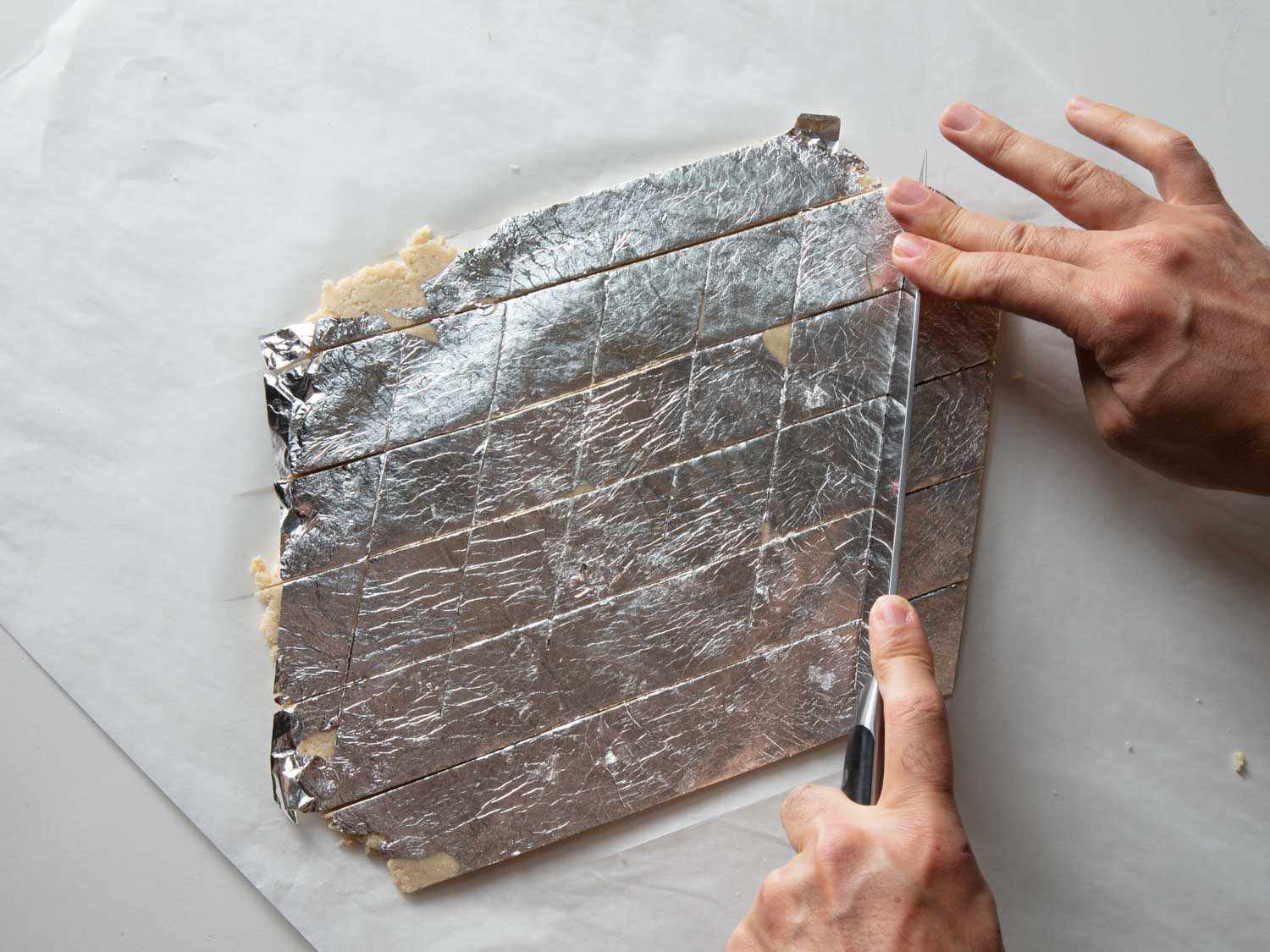 Overhead view of the silver leaf-covered dough being cut into diamonds.