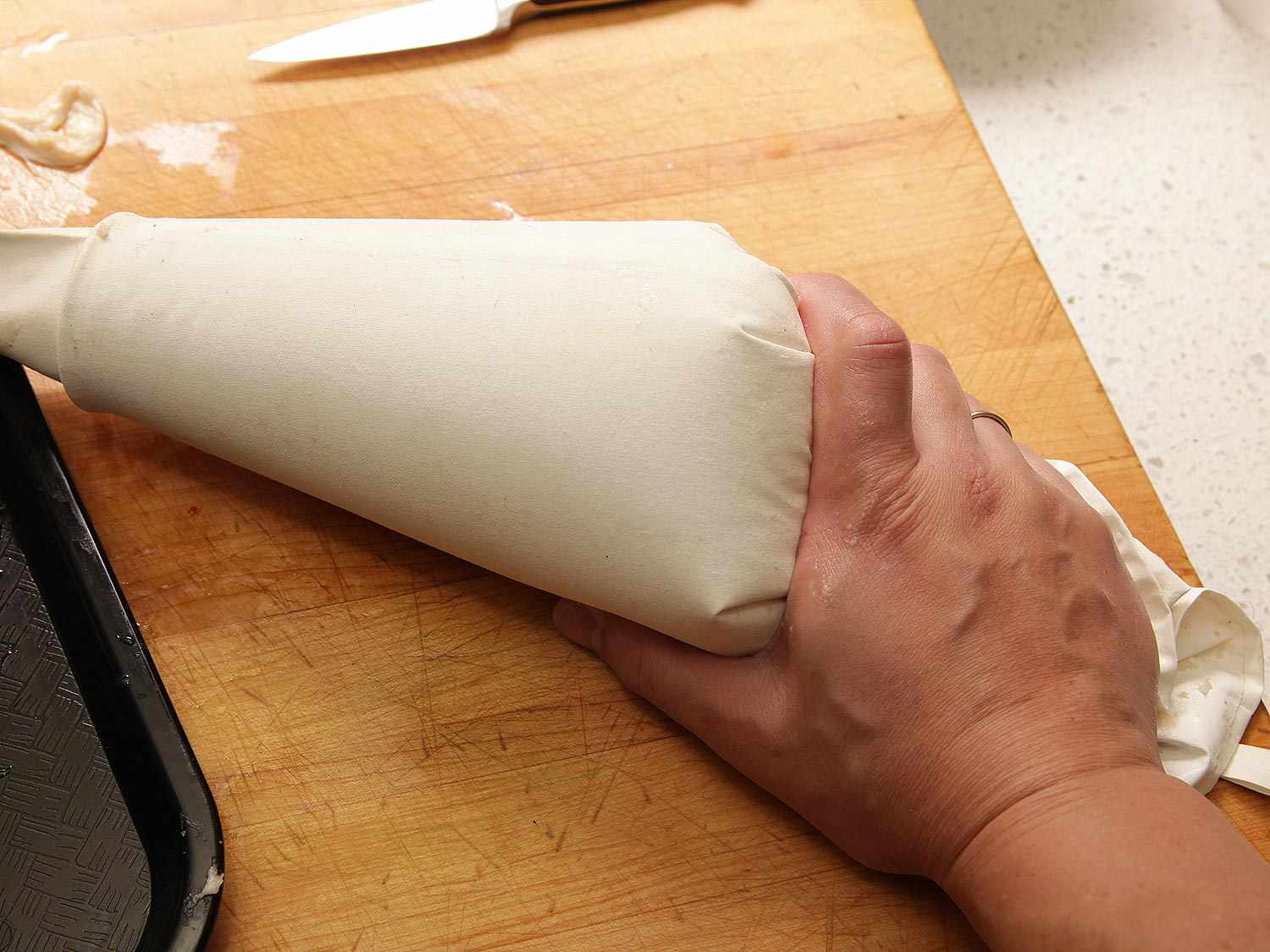 The pastry bag filled with forcemeat is pressed against a cutting board.