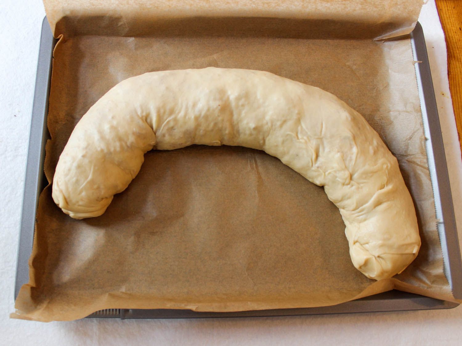 The rolled strudel is bent into a crescent shape to fit on the parchment-lined baking sheet.