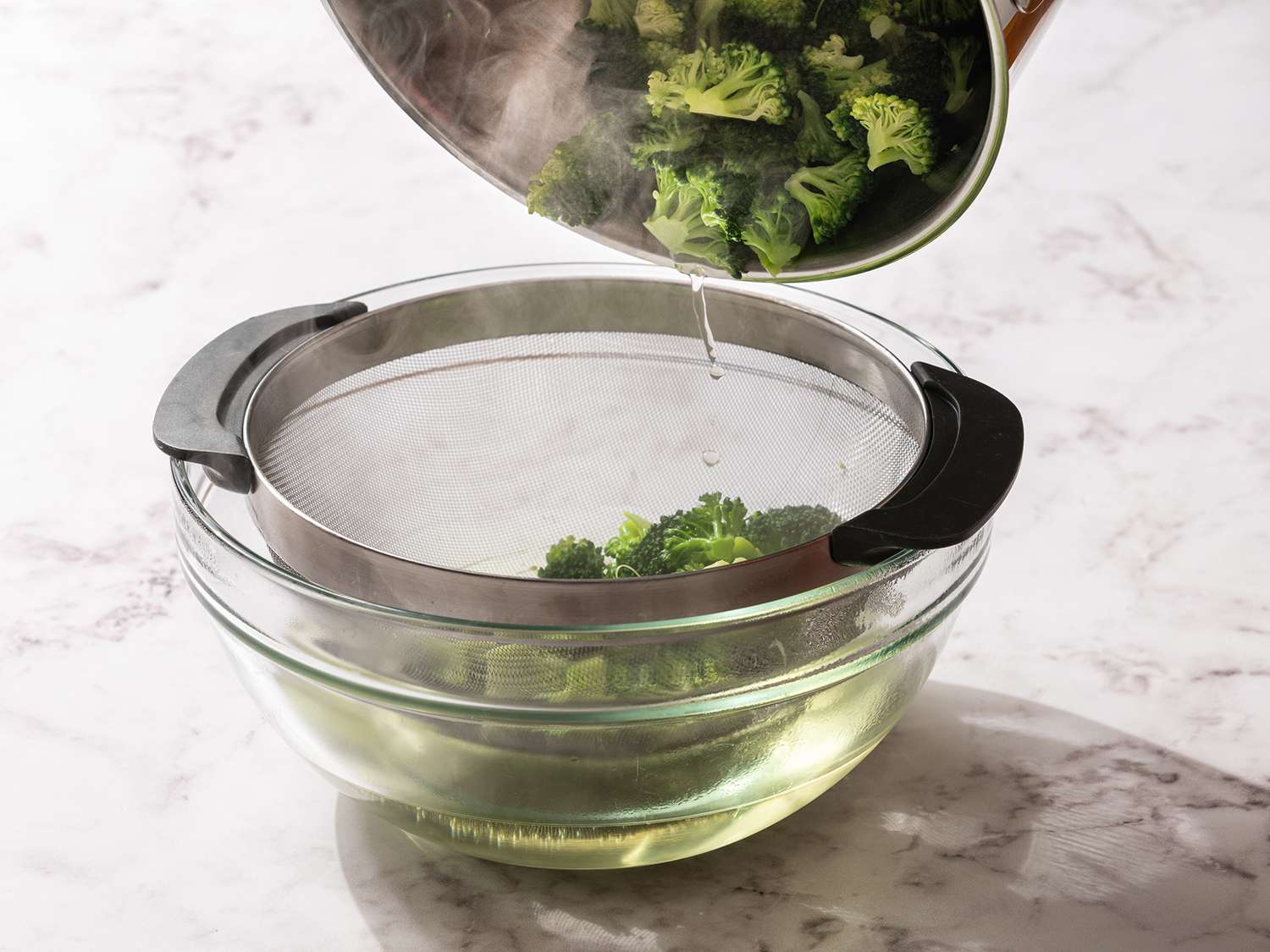 Broccoli drained over a fine mesh strainer, into a glass bowl 