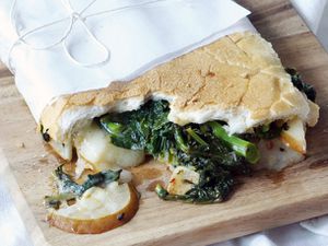 Closeup of a half-eaten Broccoli Rabe, Pear, and Fontina Sandwich. The sandwich has been wrapped in a wax paper "diaper."