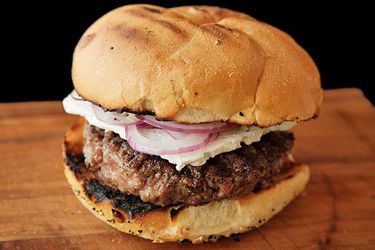 a lamb burger topped with feta and sliced red onions on a grilled bun. 