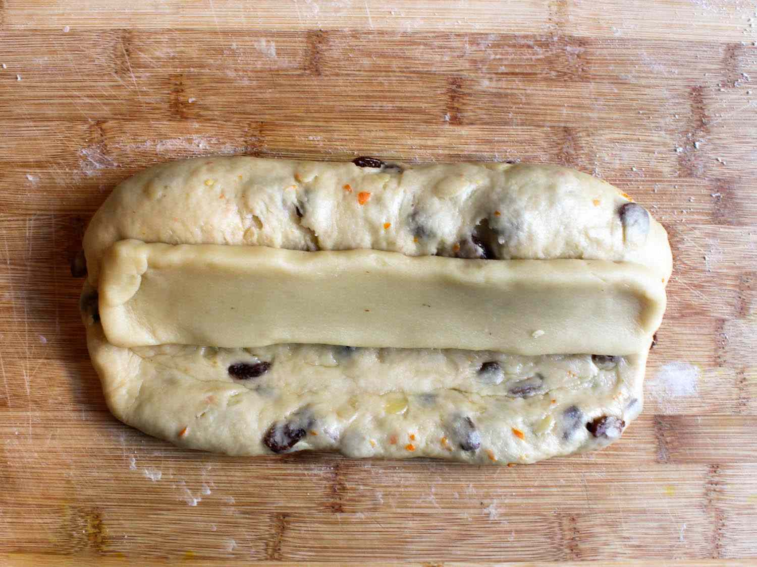 Uncooked stollen dough with a log of marzipan in the middle, on a wooden work surface.