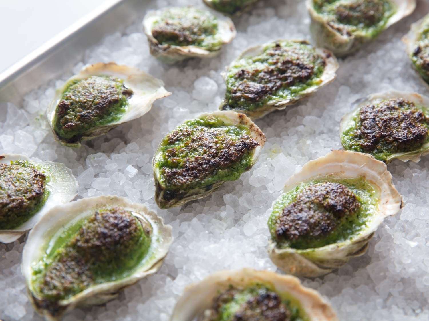Oysters Rockefeller (broiled oysters with herb/butter sauce) lined up on a rock salt-covered sheet pan.