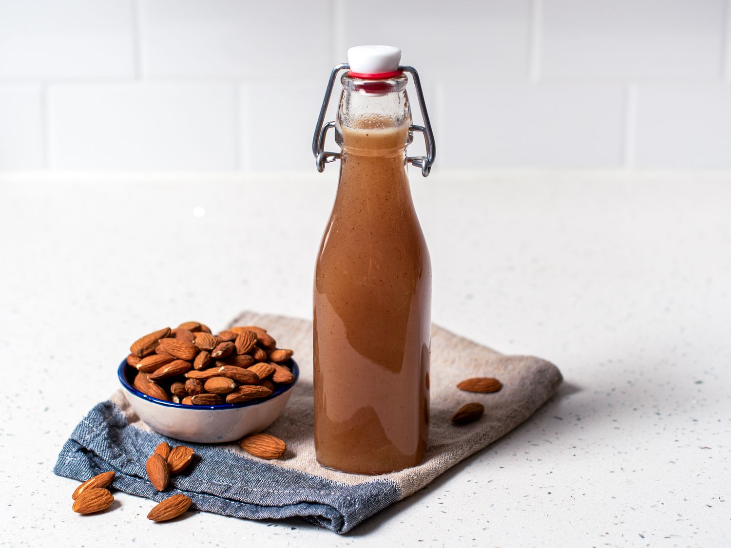 A bottle of DIY Orgeat next to a bowl overflowing with almonds. 