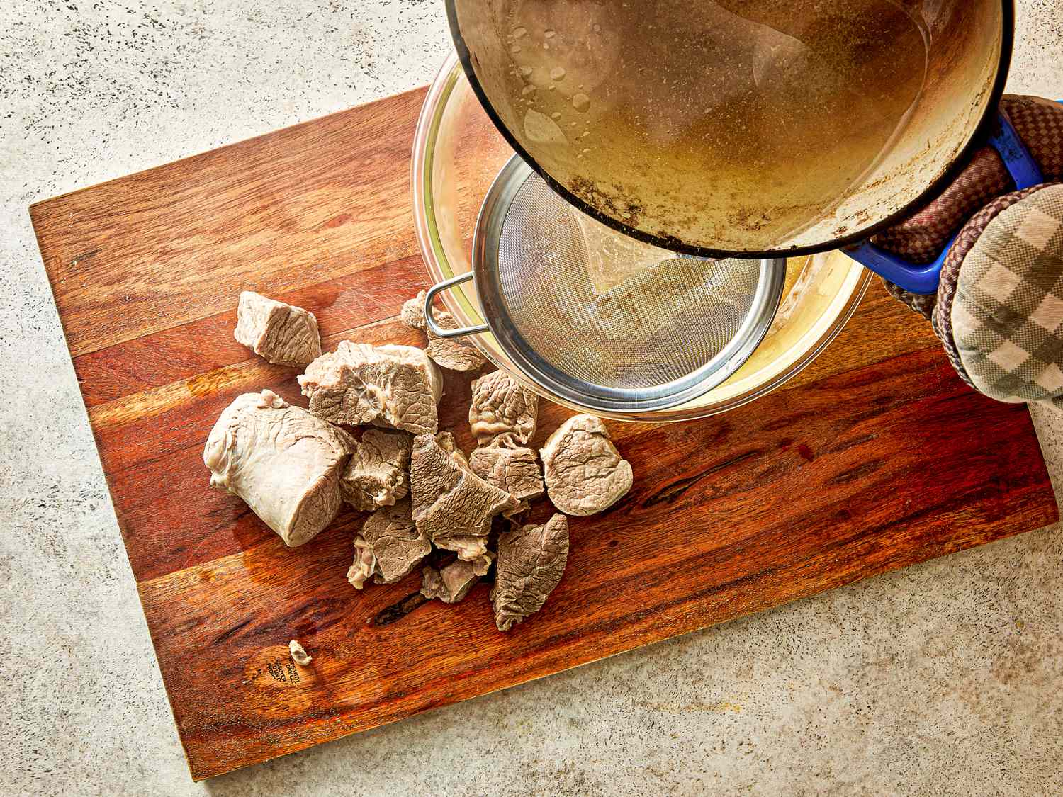 Straining cooking liquid from pieces of meat placed on a wooden cutting board