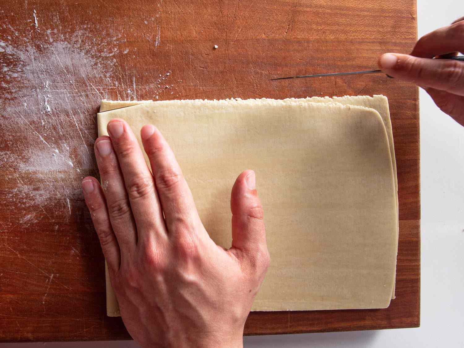 Overhead view of a doubled over sheet of ramen dough with the corner of the seam side being cut at an angle with a paring knife