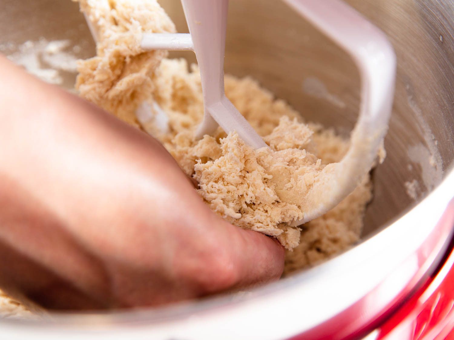 A hand freeing dough stuck to a stand mixer paddle